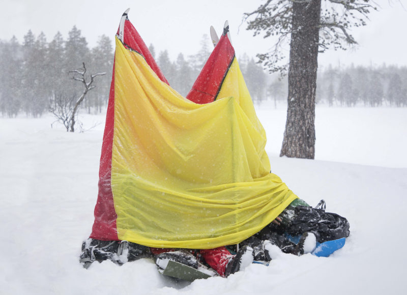 En vindsäck i gult och rött skyddar personer i snöigt landskap.