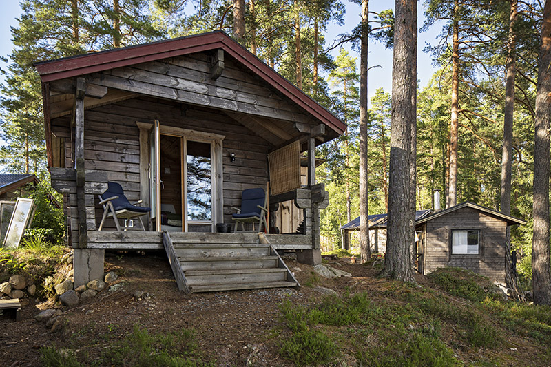 En grå timrad stuga med två fåtöljer på altanen på Nätsjö udde.