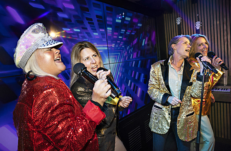 Fyra kvinnor i glittriga kavajer sjunger karaoke.