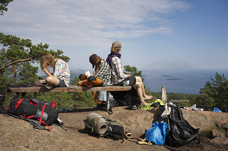 Två barn sitter på en bänk och läser. En kvinna tittar ut över havet och njuter av utsikten i Skuleskogen.