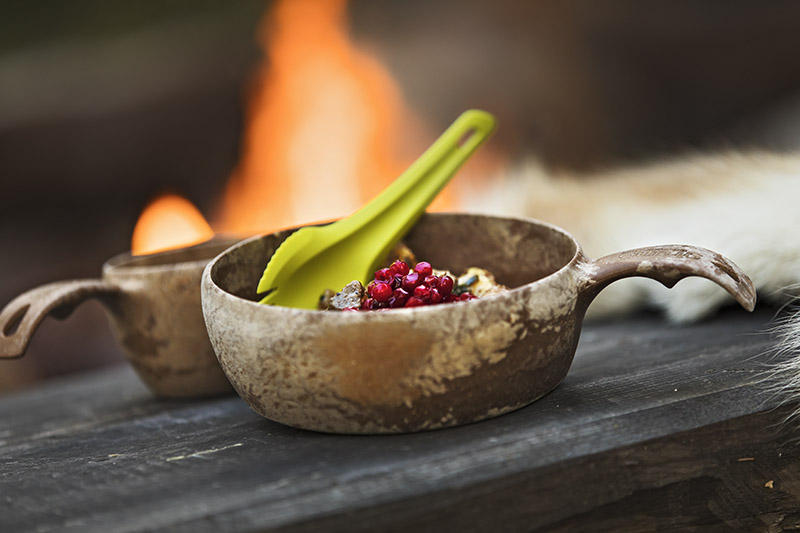 Detaljbild av en kåsa med lingonsylt och en grön plastsked.