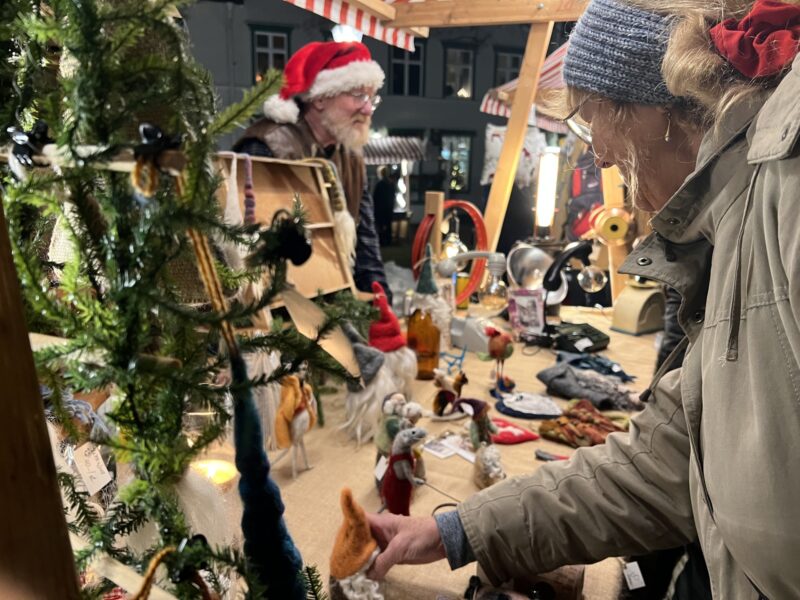 Besökare tittar på tovade tomtar i ett stånd på en julmarknad.